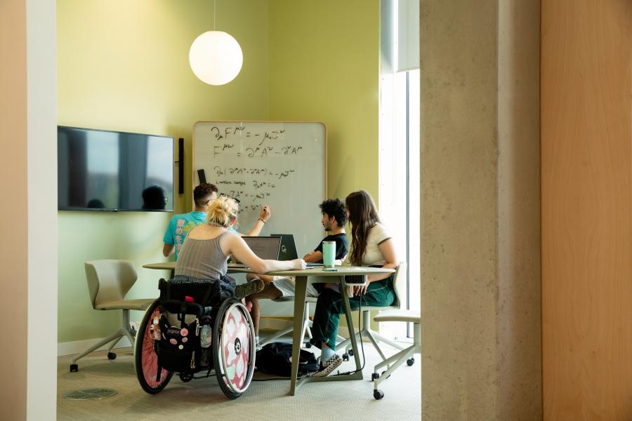 Four students studying around a table, with a whiteboard next to them