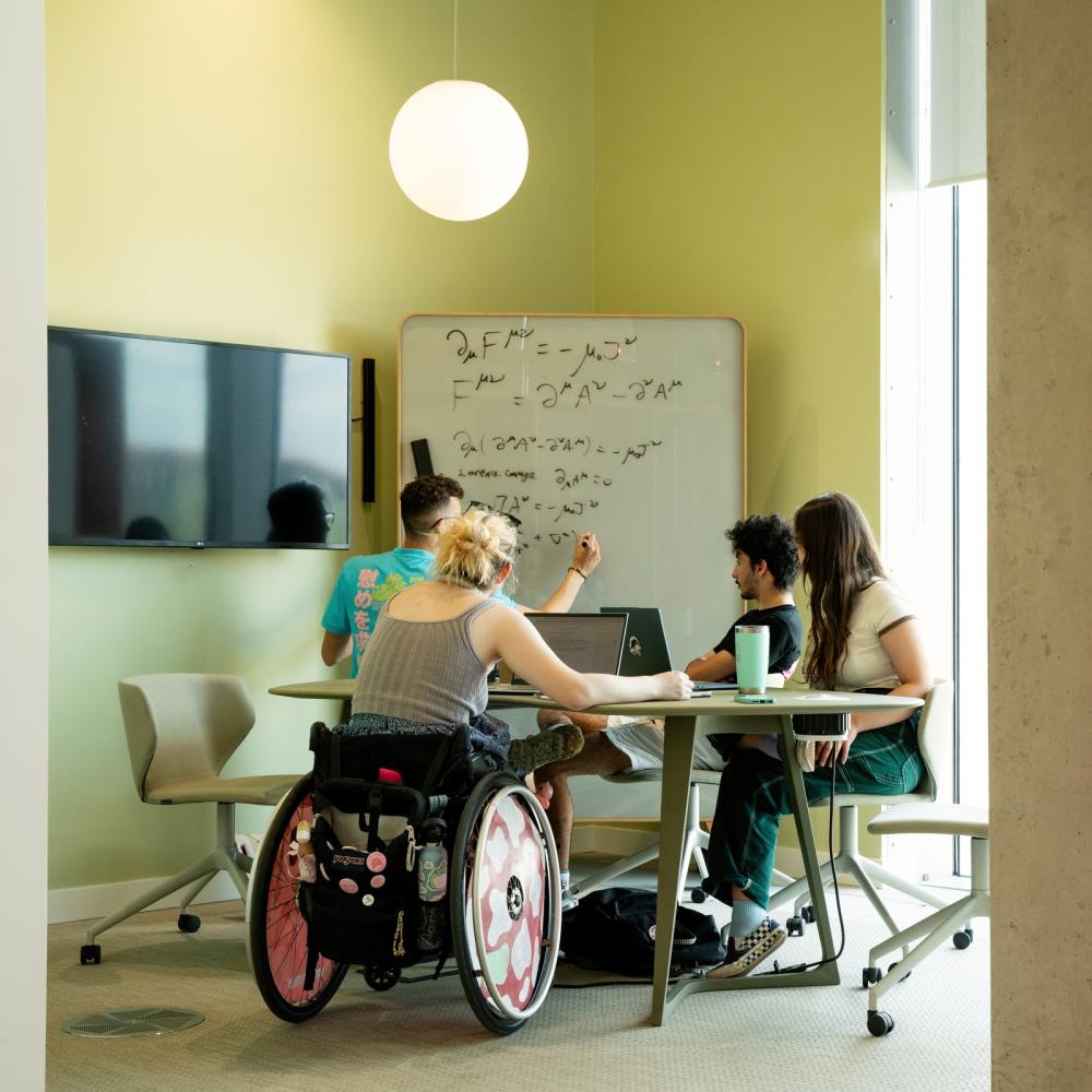 Four students studying around a table, with a whiteboard next to them